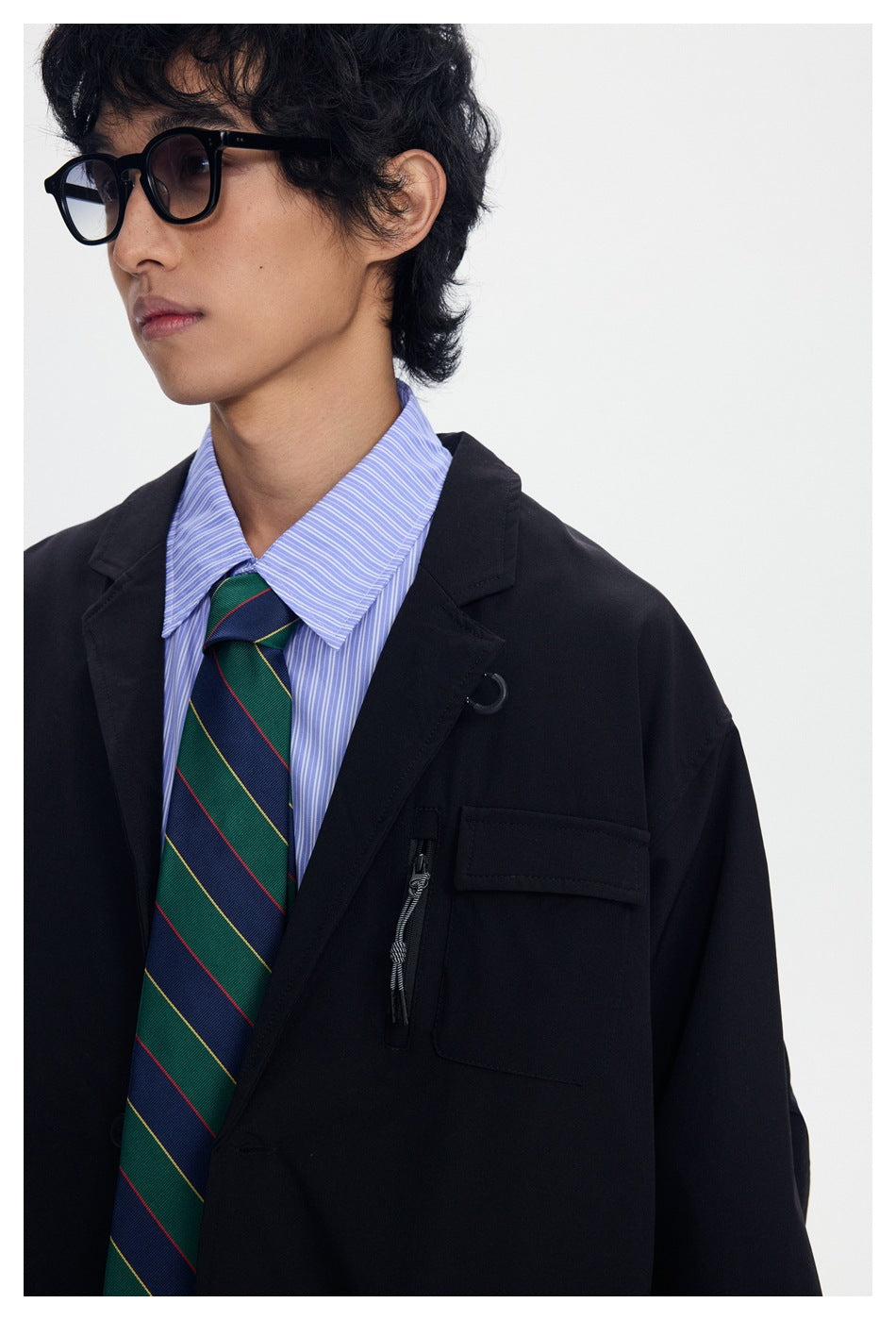 Close view of a model wearing a black blazer with a flap chest pocket and vertical zip pocket over a striped shirt and tie.