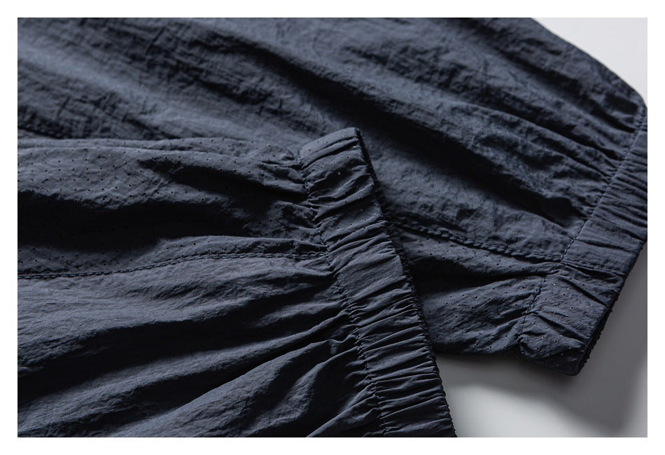 Close-up of a dark jacket showing gathered elastic edging, stitched seams, and perforated fabric panels.