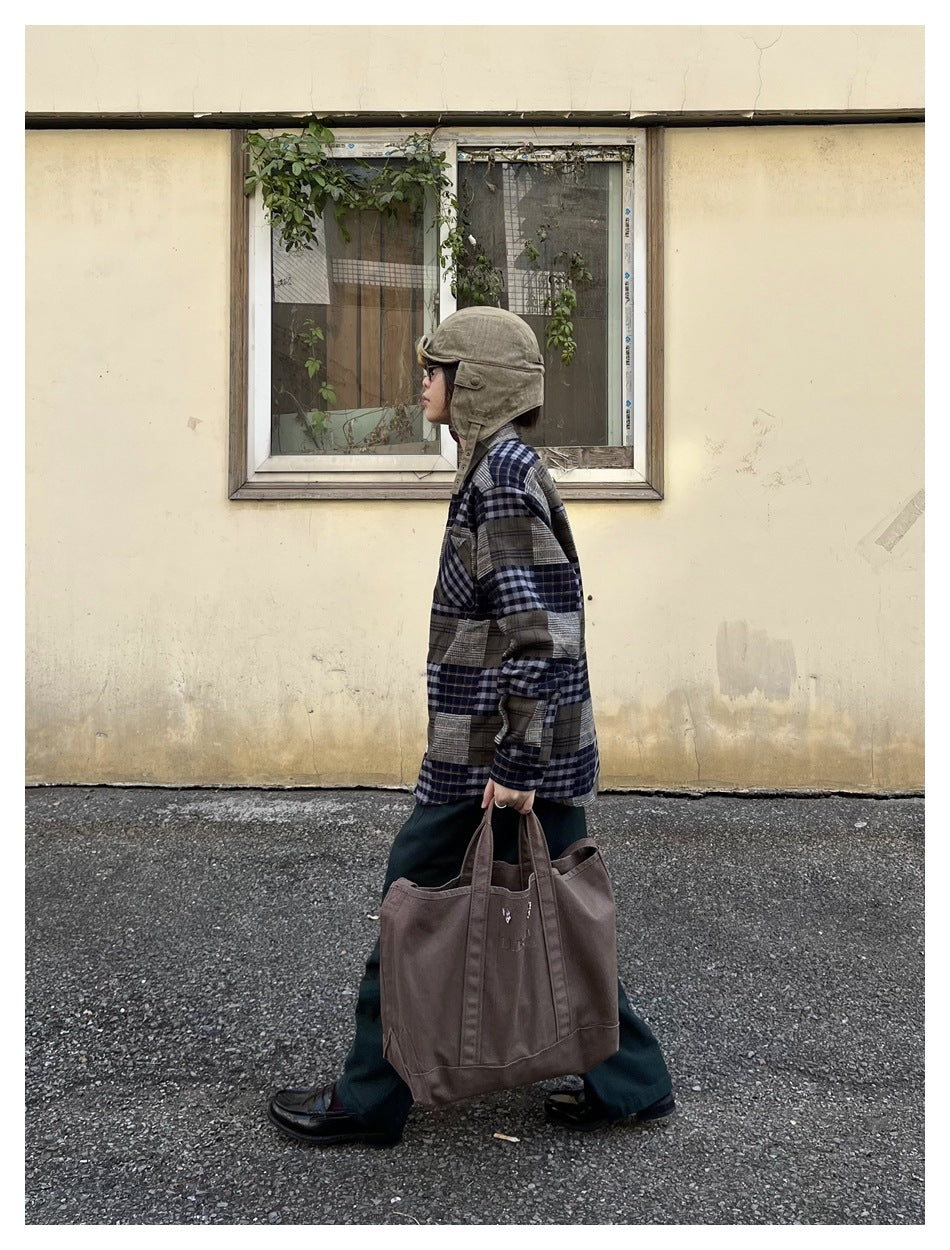 Side view of a person wearing the patchwork plaid shirt with a hat, dark trousers and a canvas tote bag
