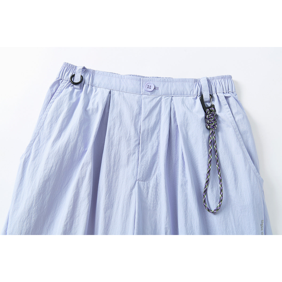 Close-up of pale lavender pants with a gathered waistband, button closure, pleats, belt loops, and a hanging braided cord.