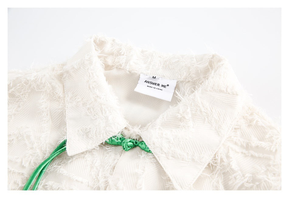 Close-up of an ivory shirt's pointed collar, textured fringed fabric, and sewn-in neck label.