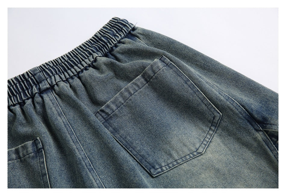 Angled close-up of a back patch pocket and gathered elastic waistband on blue-gray washed denim shorts.