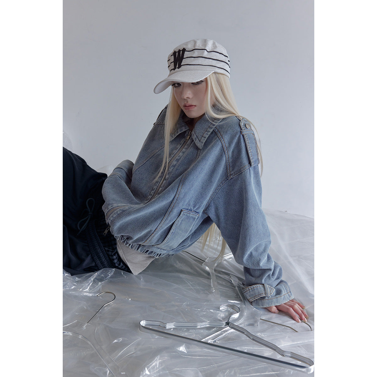 Seated model wearing an oversized blue denim jacket with a zip front, wide sleeves and shoulder tabs.