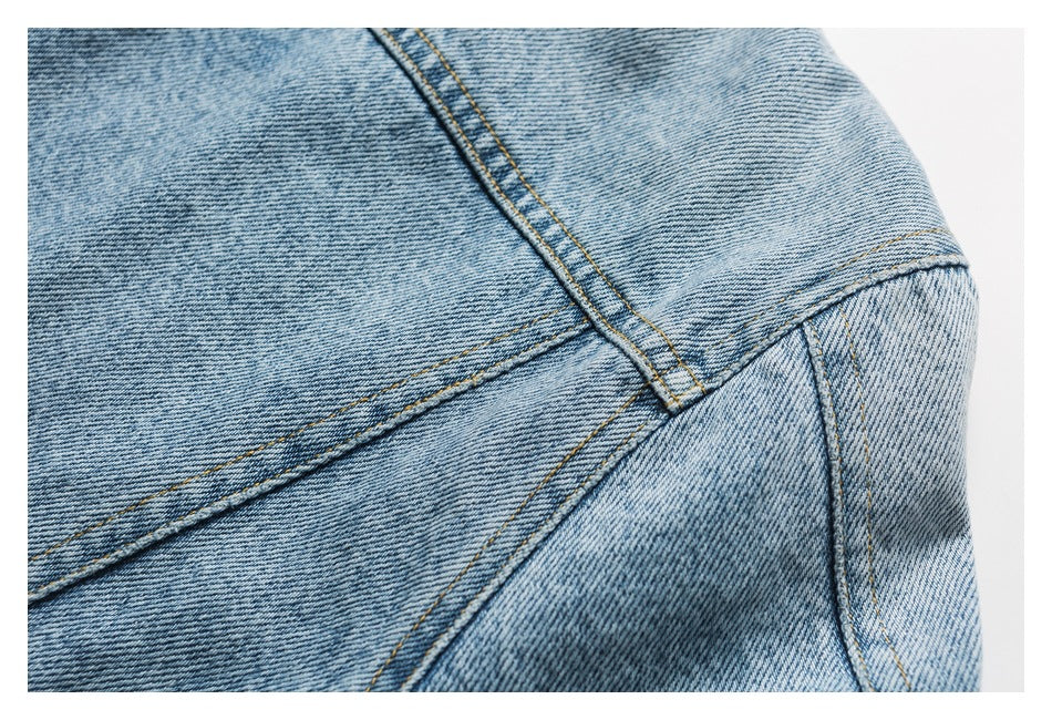 Close-up of light blue denim with intersecting seams and golden-brown stitching.