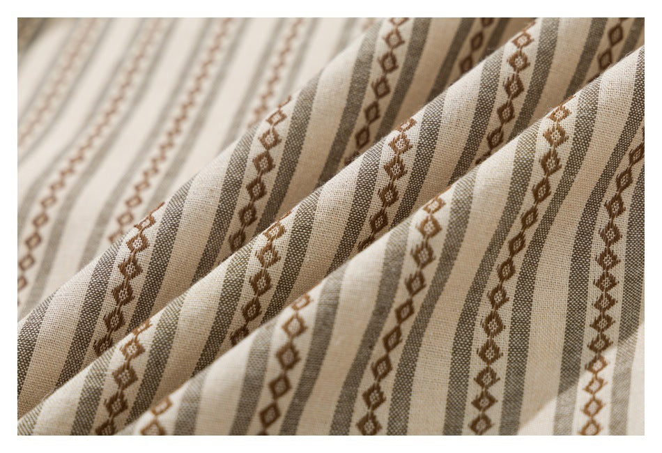 Macro view of beige fabric with alternating taupe stripes and brown geometric motifs, draped in folds.