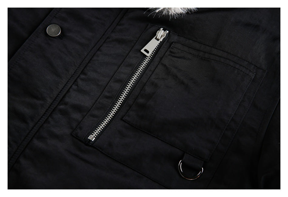 Close-up of a black jacket with a silver zipper pocket, snap button, metal ring, and a small fur-trimmed edge.