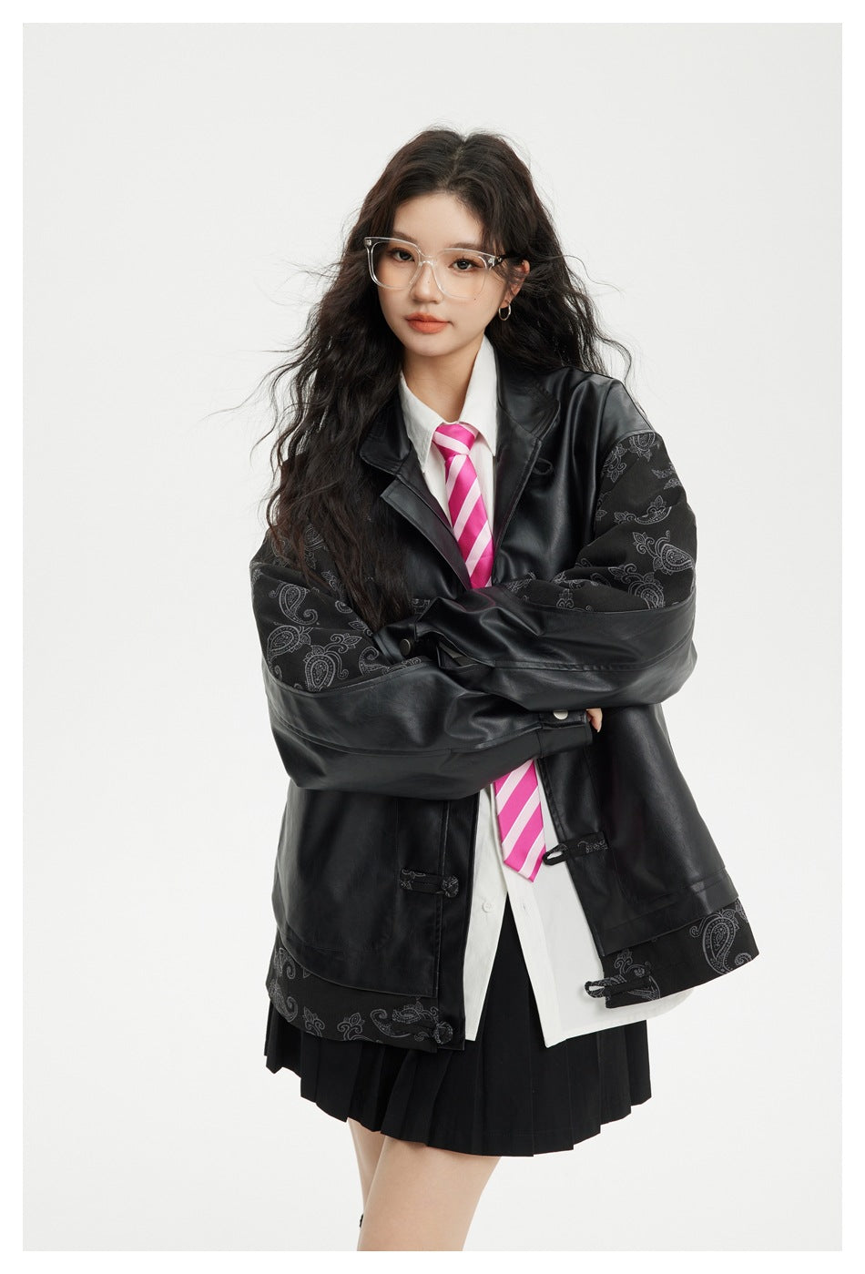 Model wearing an oversized black jacket with paisley-patterned panels, frog closures, and a white shirt with a pink striped