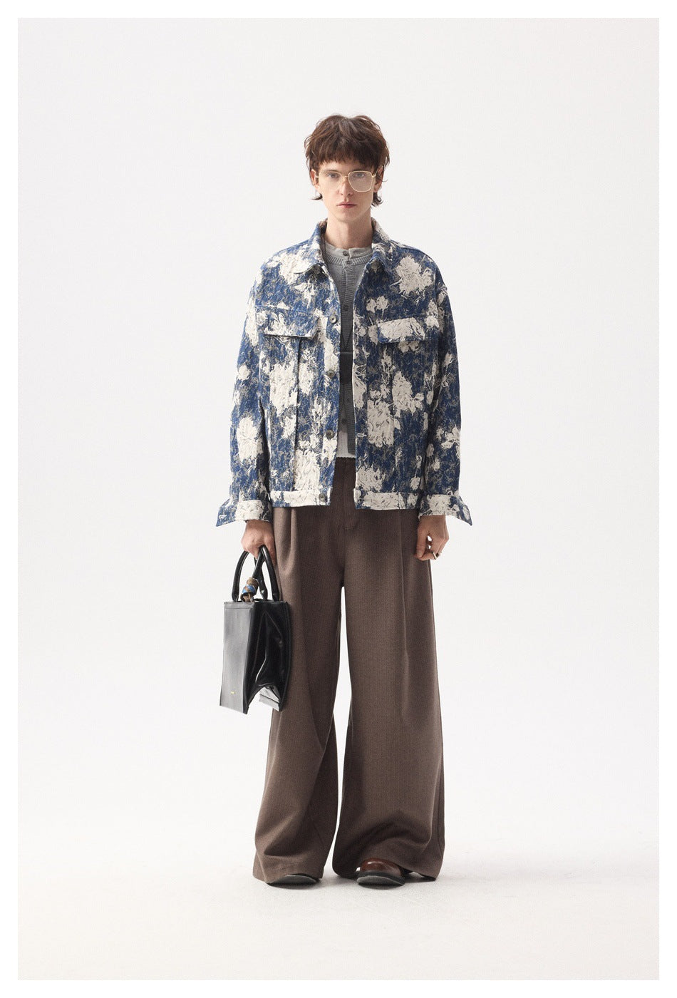 Model wearing a blue and cream floral jacket over a gray knit top with brown wide-leg pants, holding a black bag