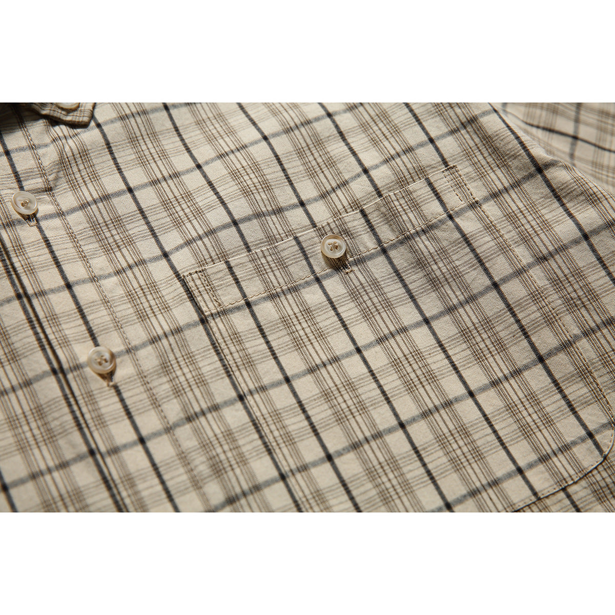 Close-up of the beige plaid shirt’s chest pocket, stitching, buttons, and intersecting dark lines.