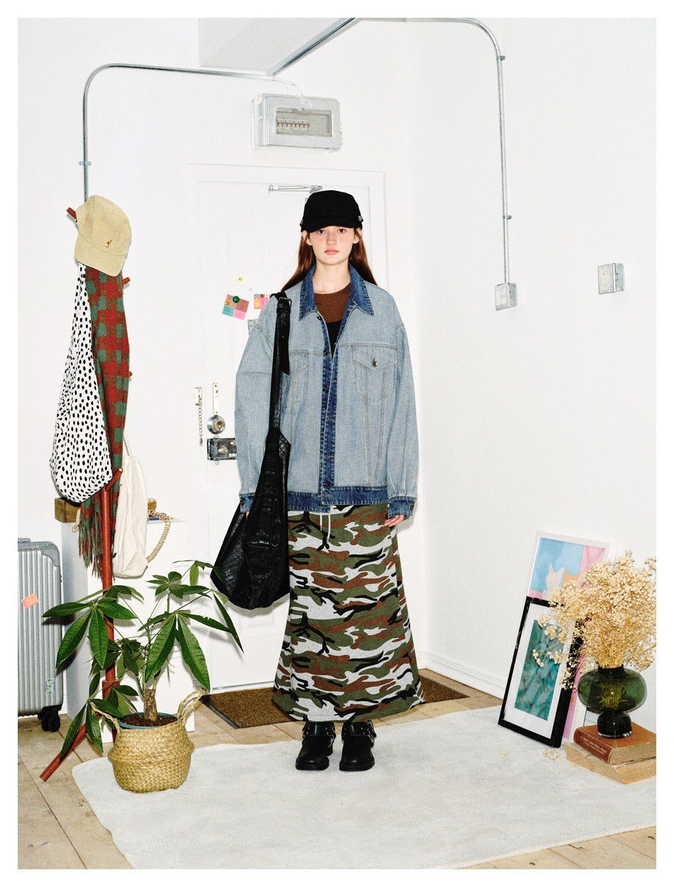 Front view of a model wearing an oversized light blue denim jacket with dark denim trim and a camouflage maxi skirt.