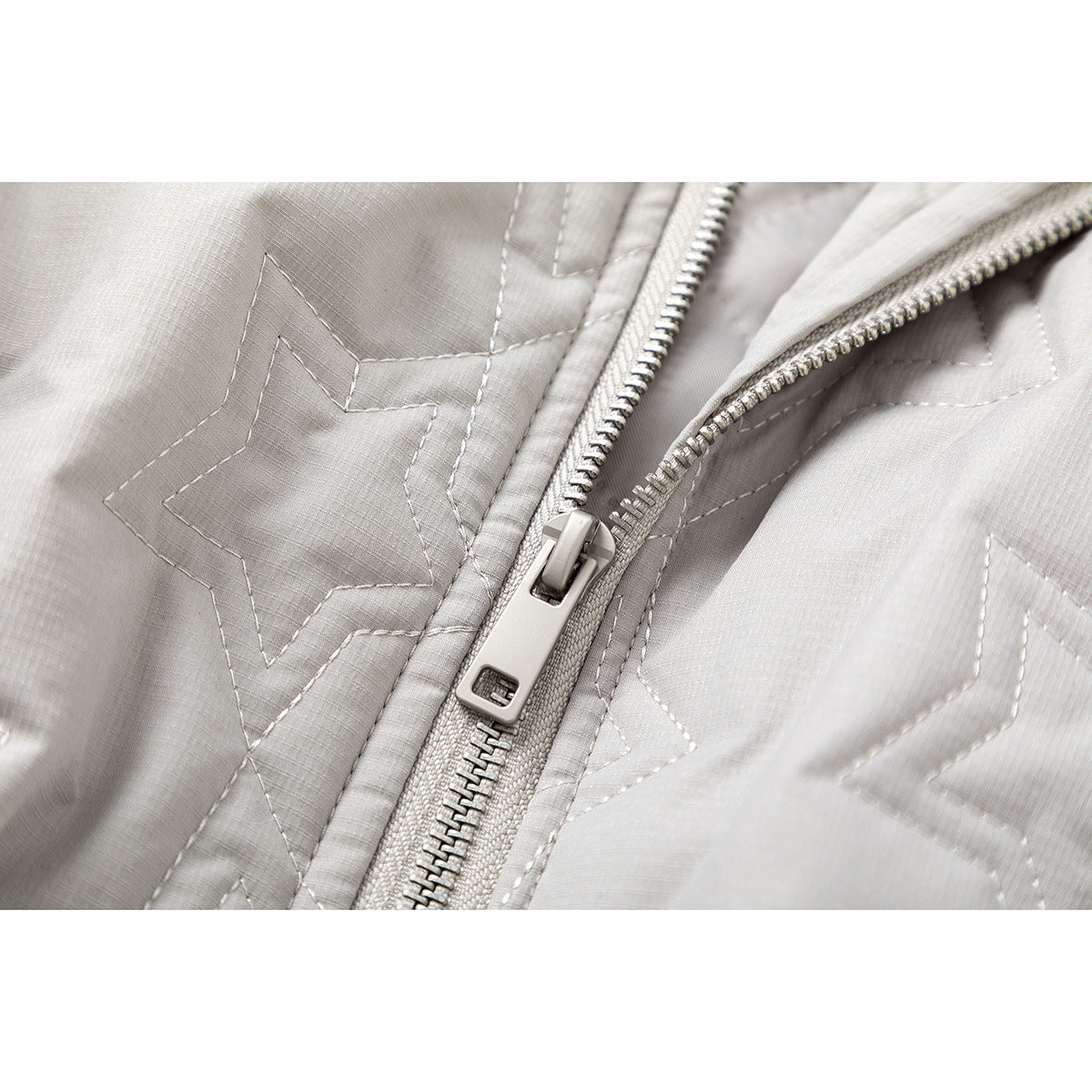 Close-up of the light gray jacket's front zipper and stitched star quilting.