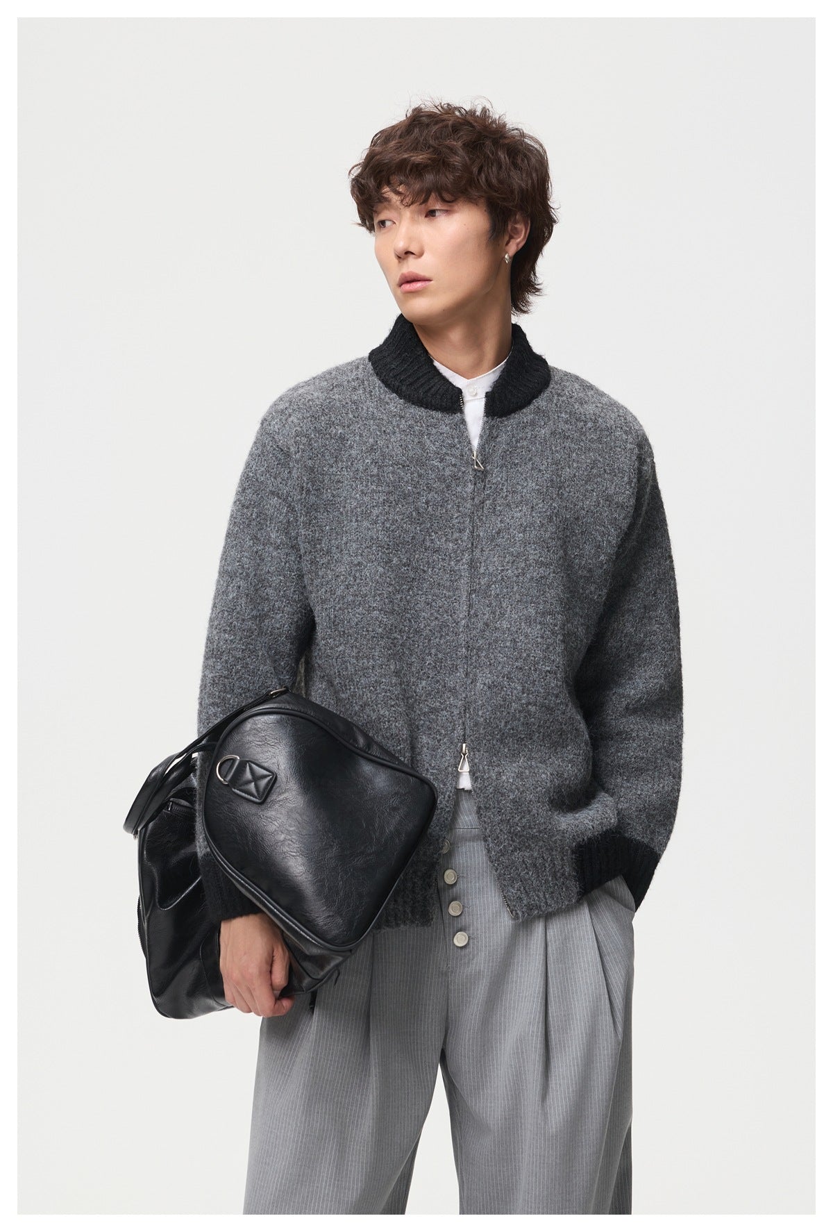 Model wearing a dark gray knit jacket with black ribbed trim, holding a black shoulder bag.