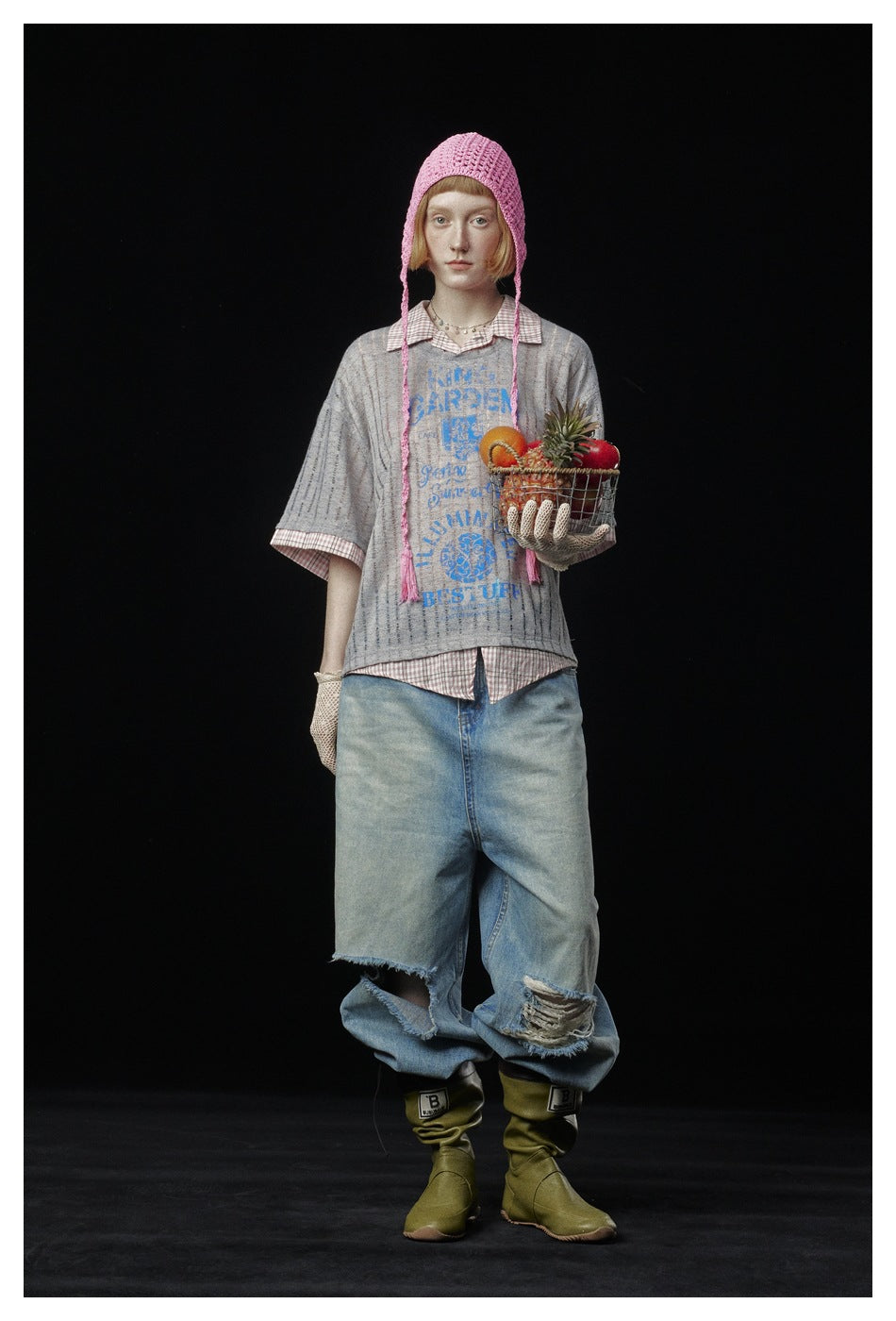 Front view of a model in a gray striped graphic top, checked shirt, pink crocheted bonnet and ripped loose jeans.