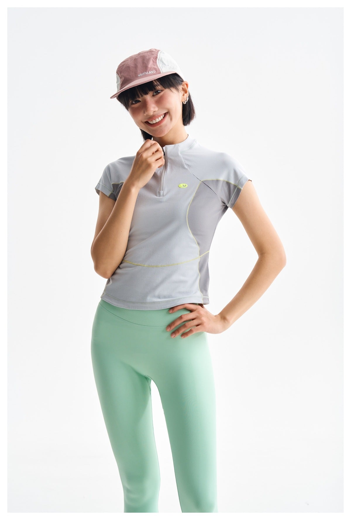 Model wearing a light gray short-sleeve quarter-zip top with lime piping and mint leggings.