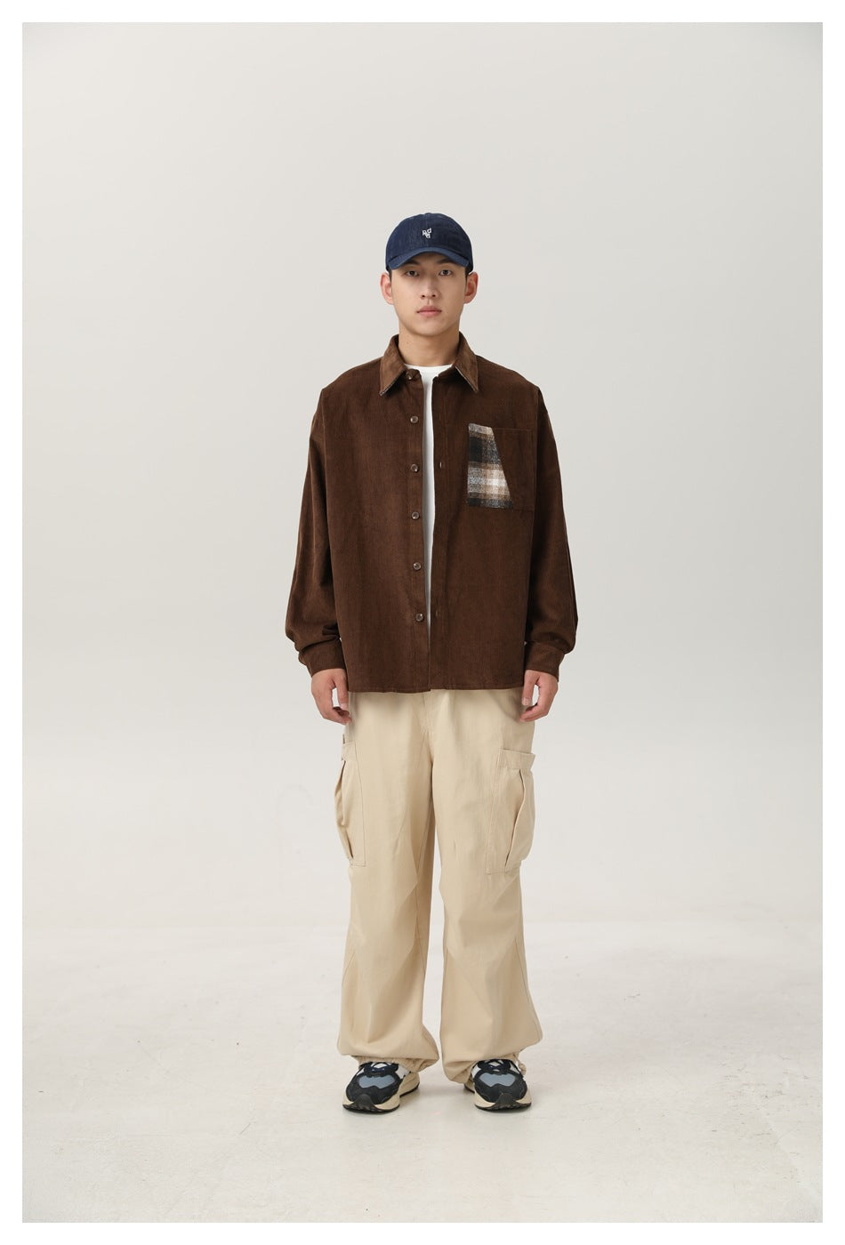 Model wearing brown corduroy shirt with plaid chest pocket panel, beige cargo pants and navy cap, front view