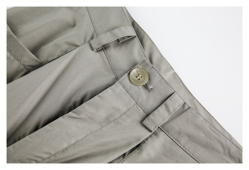 Close-up of taupe-gray trousers showing a waistband button, belt loops and front pleats.
