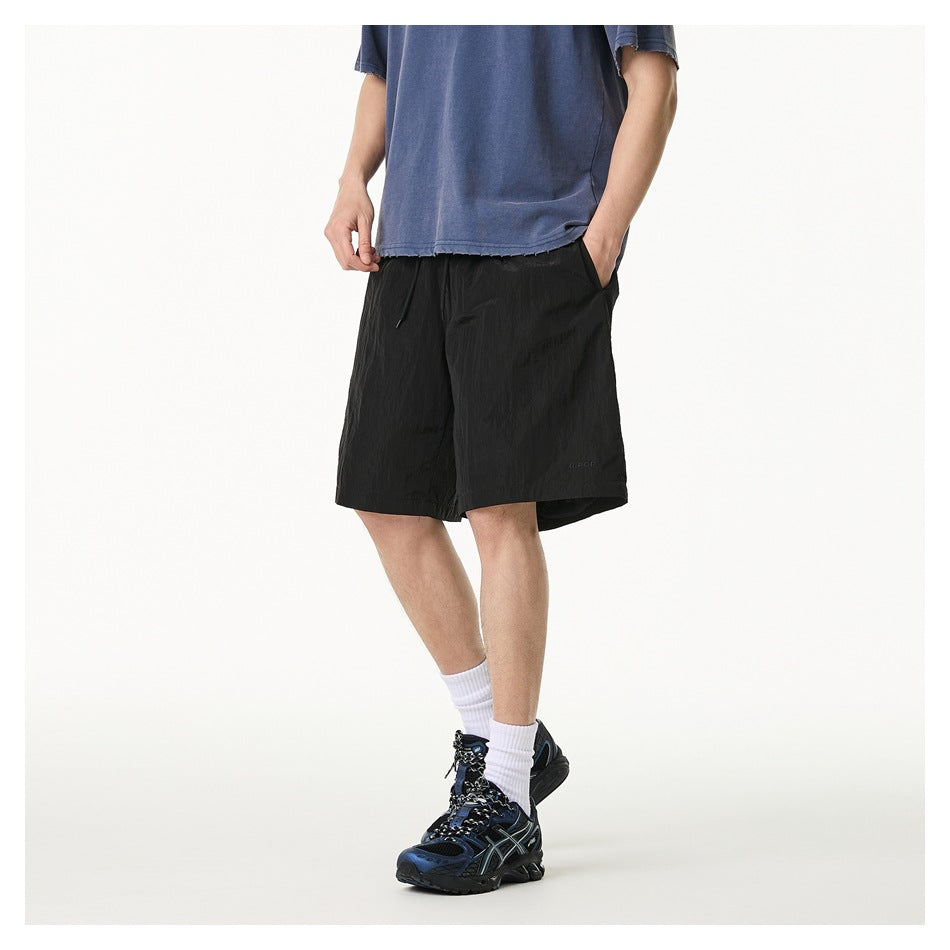 Angled front view of a model wearing loose black knee-length shorts with a drawstring and pockets.