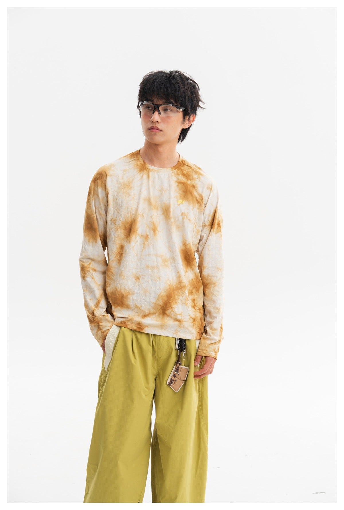 Model wearing a cream long-sleeve shirt with ochre tie-dye patterns and loose yellow-green trousers.