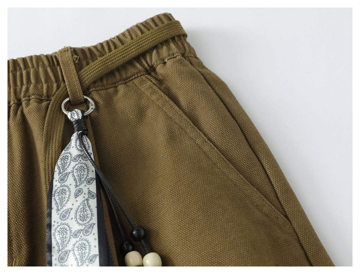 Close-up of the olive-brown trousers' elastic waist, drawstring, angled pocket and paisley-patterned accessory.