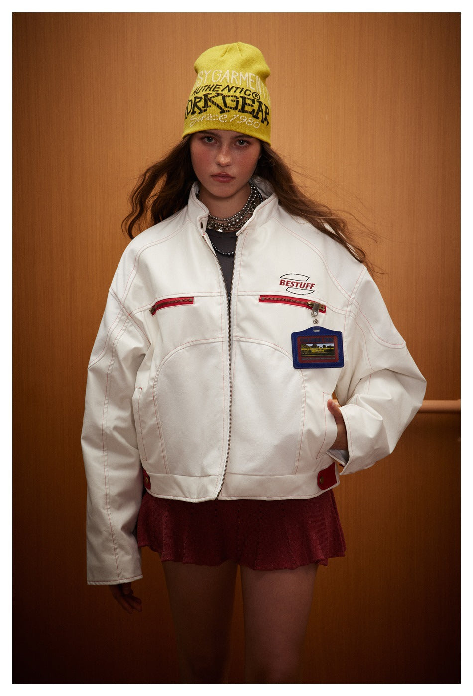 Front view of a model wearing an oversized white jacket with red zip pockets and a burgundy skirt.