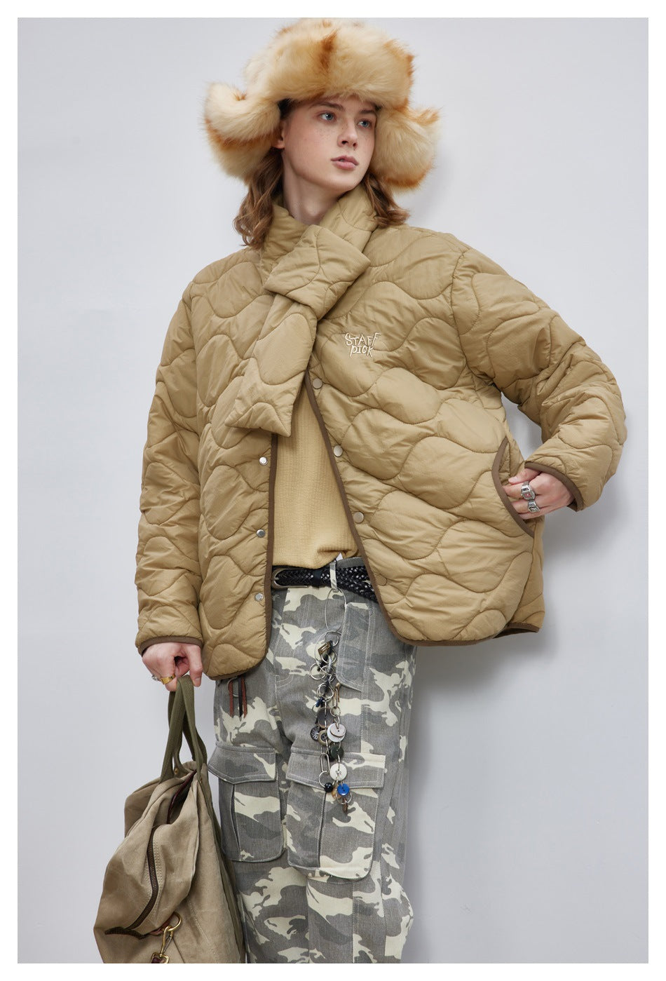 Model wearing a tan wave-quilted jacket with a padded wrap collar, shown from the front with one hand in a pocket.