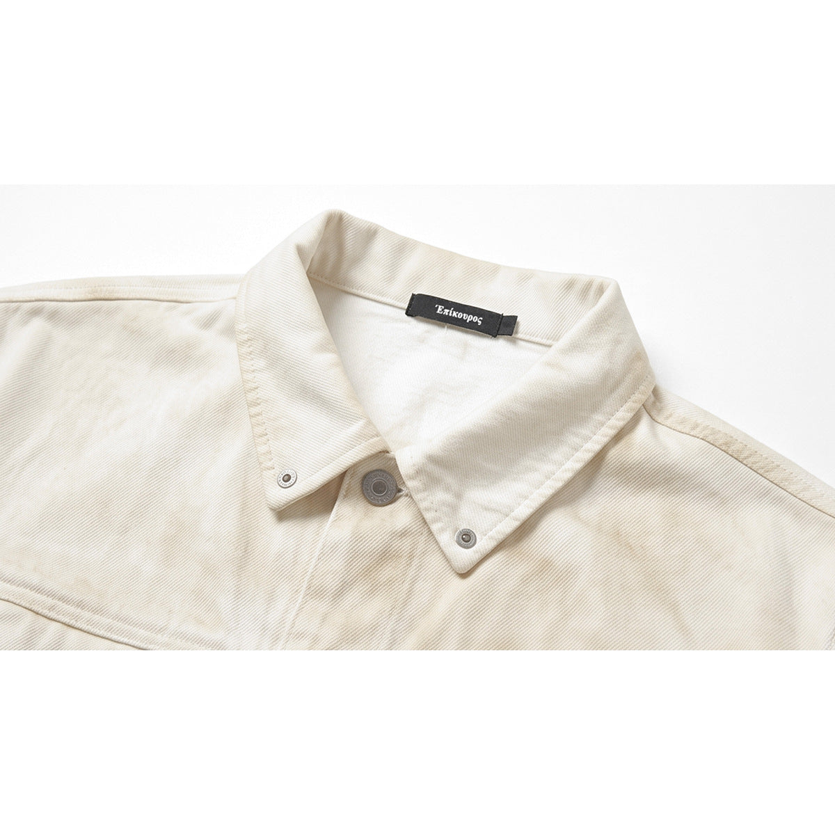 Close-up of an ivory jacket collar with metal snaps and a black Greek-text neck label.