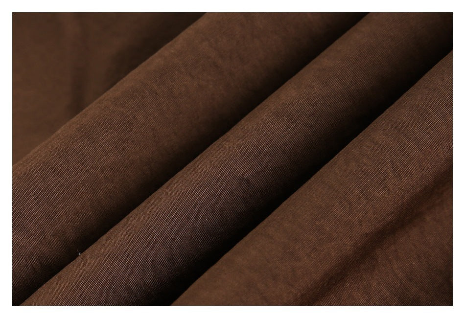 Extreme close-up of the dark brown pants fabric folded into soft diagonal ridges.