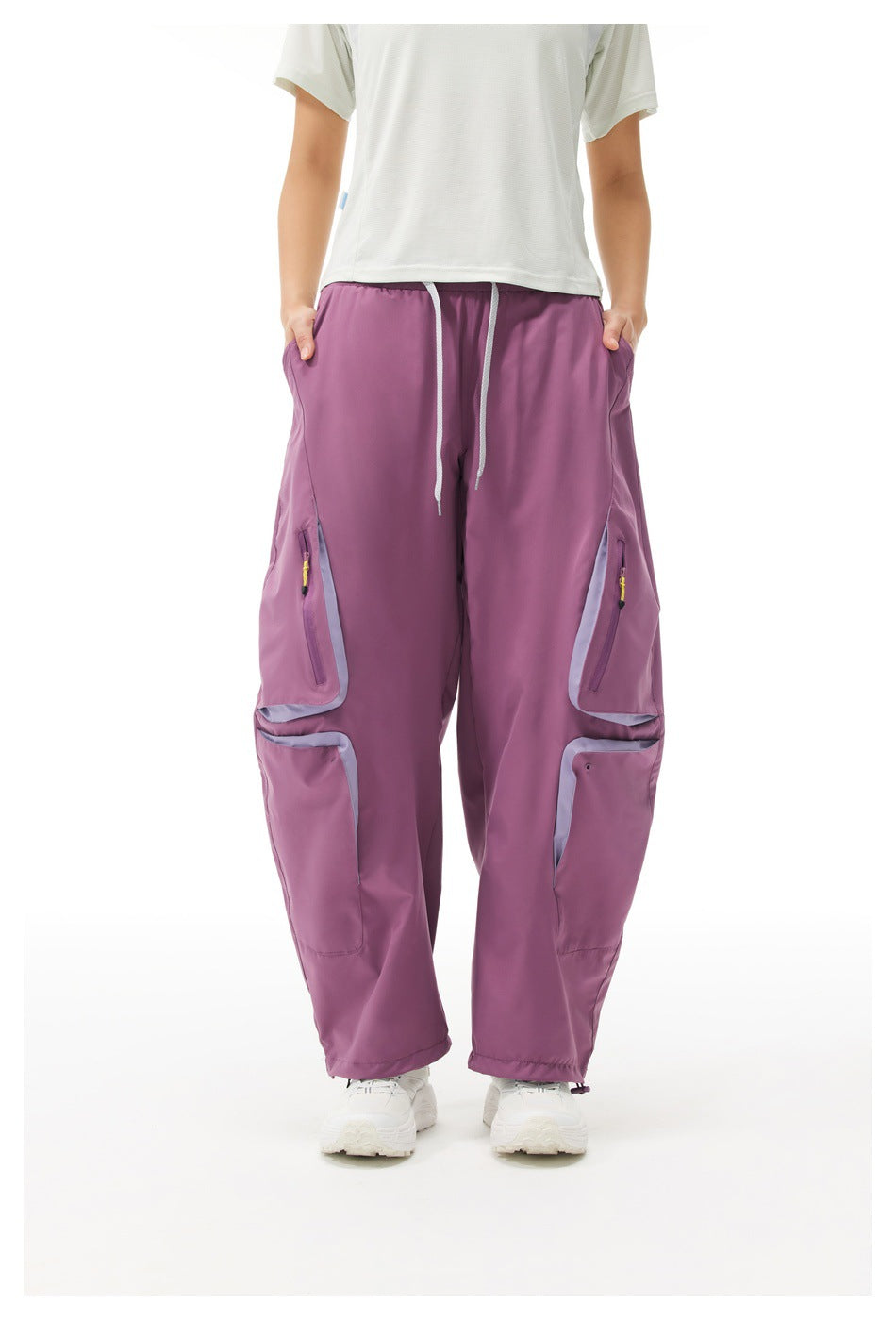 Front view of a model wearing loose plum-purple cargo pants with drawcords, zip pockets and pale trim.