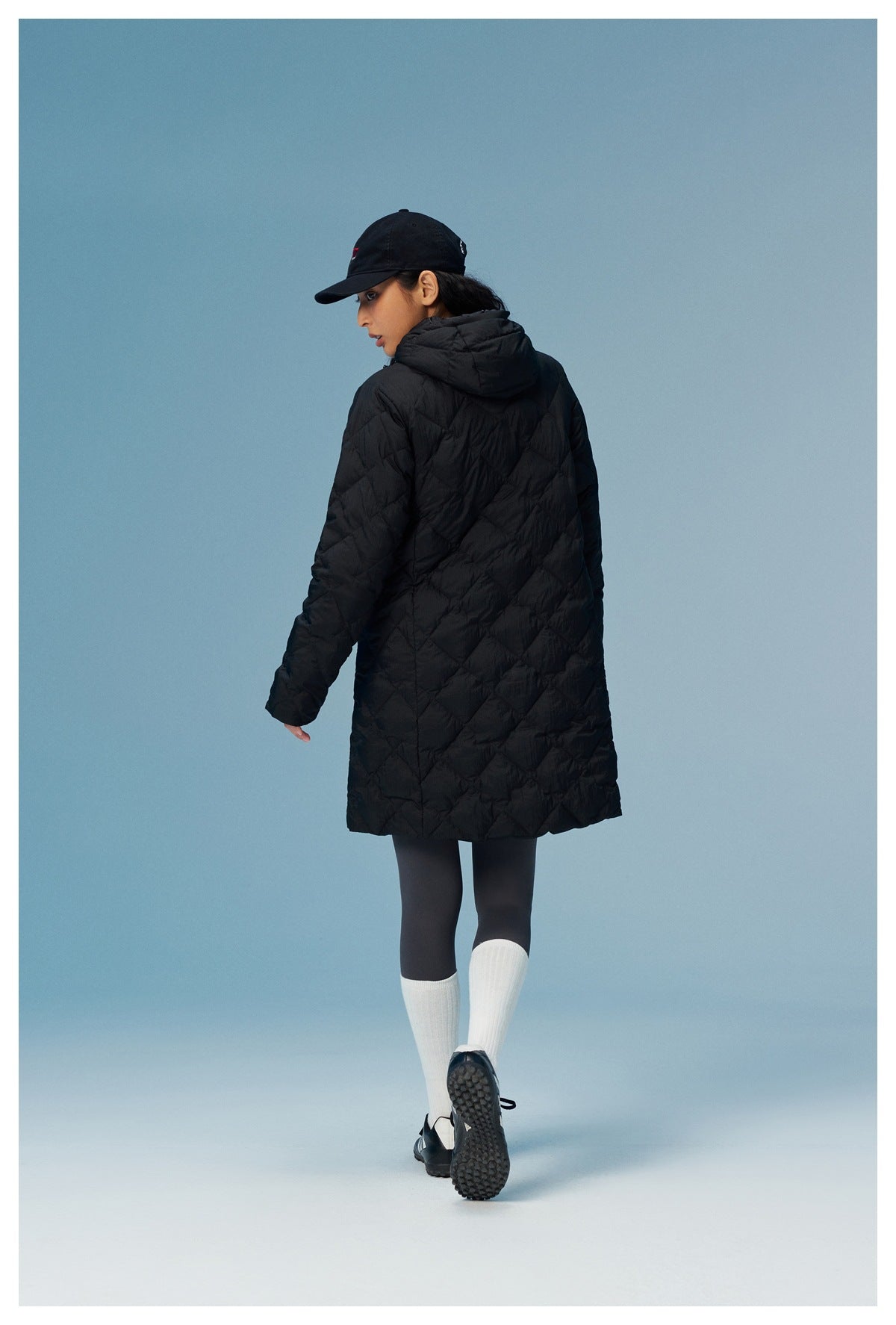 Rear view of a model wearing a black, knee-length quilted hooded coat.
