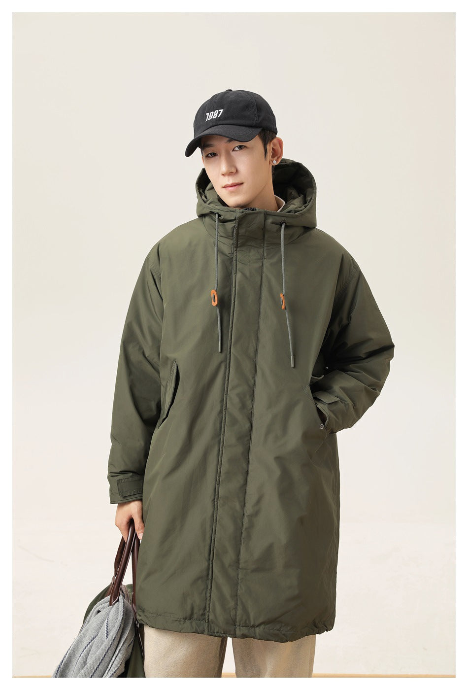 Model wearing a long olive hooded parka with front closure, drawstrings and side pockets.