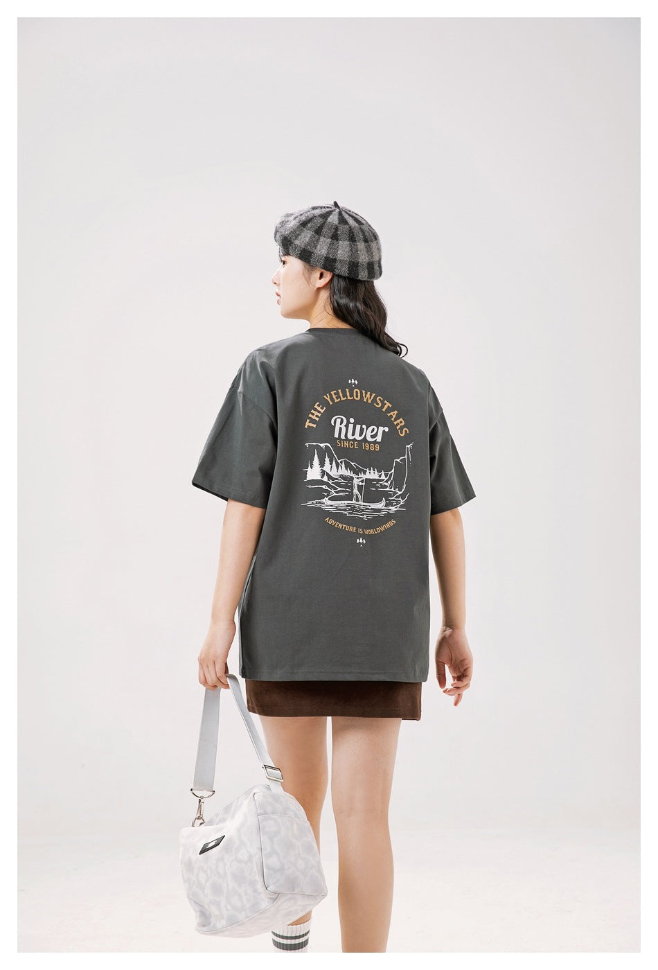 Back view of a model wearing a charcoal gray T-shirt with a large Yellowstone river graphic and English text.