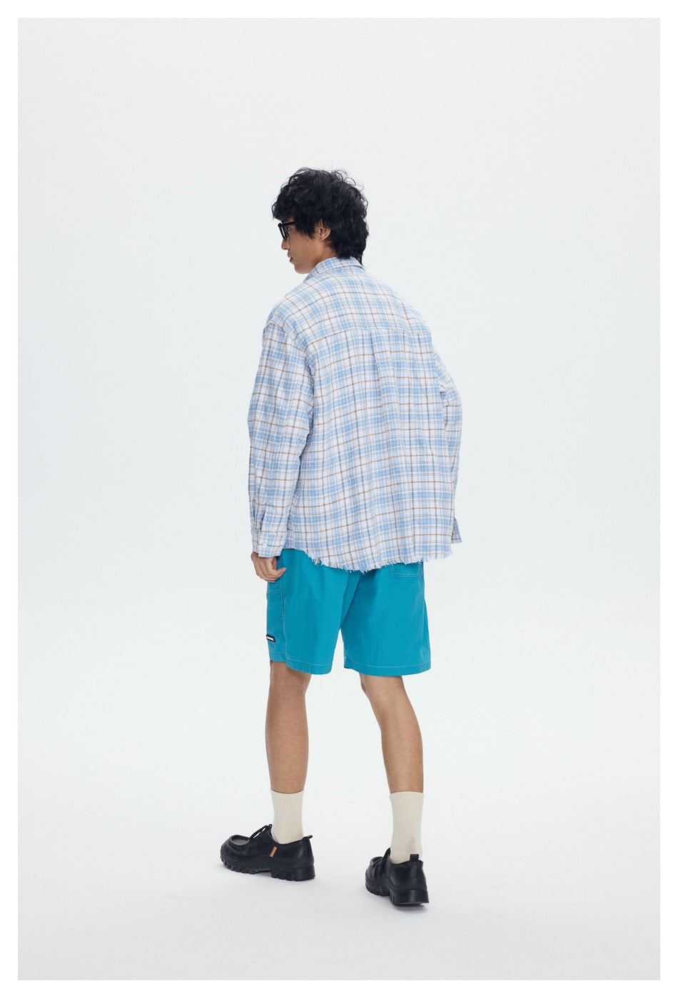 Back view of model wearing a blue plaid shirt with frayed hem and teal shorts