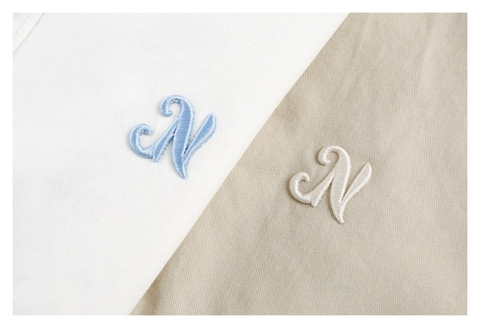 Close-up of raised letter N embroidery on white and beige jacket fabric.