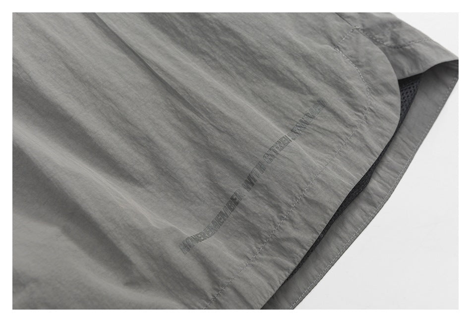 Close-up of gray shorts fabric with curved stitching and small dark English lettering printed near the hem.
