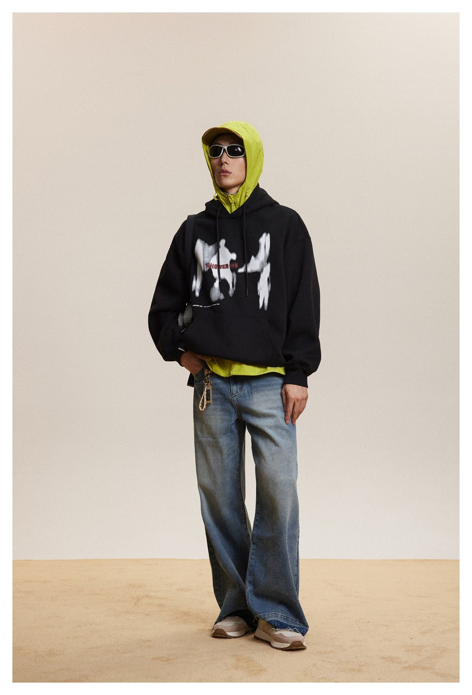 Model wearing a black hoodie with a white chest graphic, layered over a neon yellow hooded jacket.