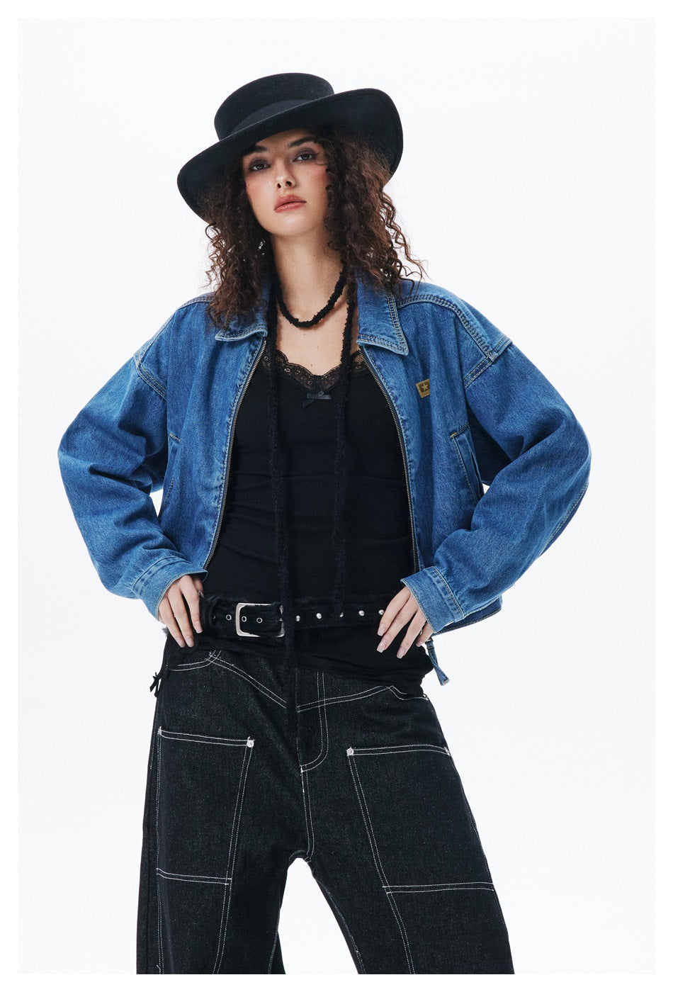 Model wearing a cropped blue denim jacket over a black top and wide-leg black jeans, shown from the front.