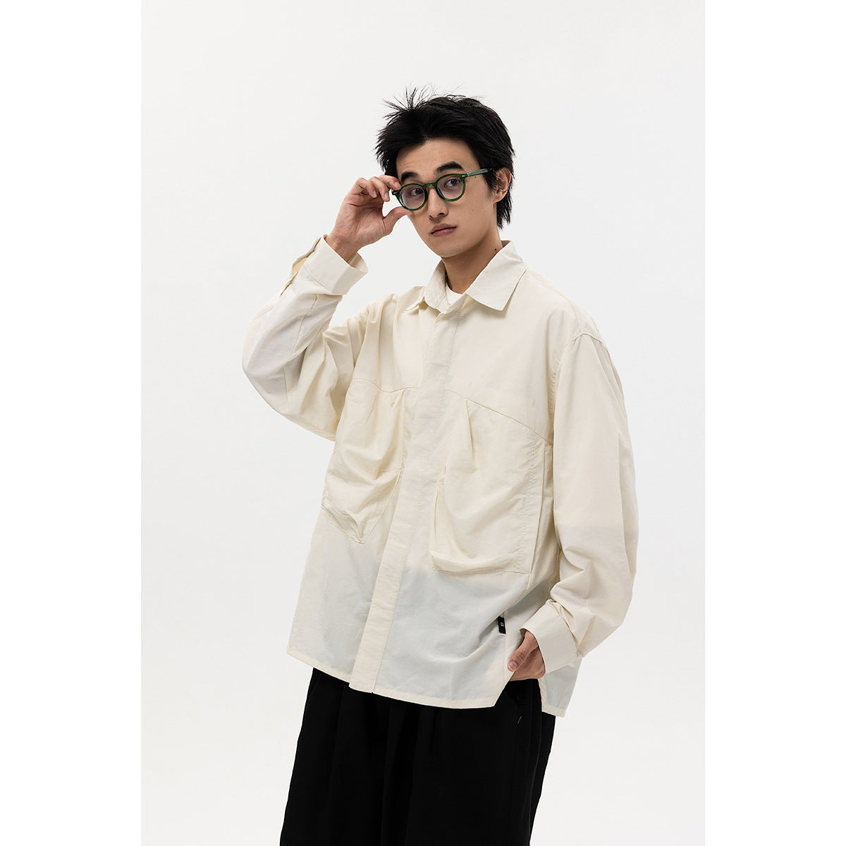 Model wearing an oversized ivory button-up shirt with two large patch pockets and black trousers.