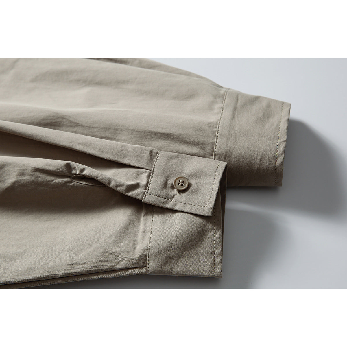 Close-up of a taupe shirt sleeve and buttoned cuff laid flat.