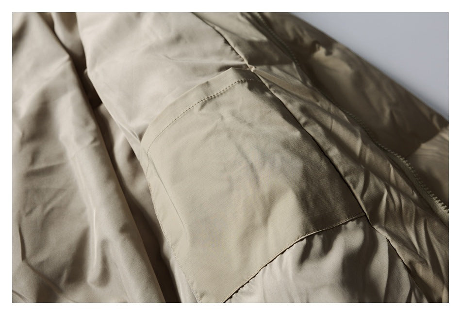 Close-up of a stitched patch pocket on the taupe jacket beside its front zipper.