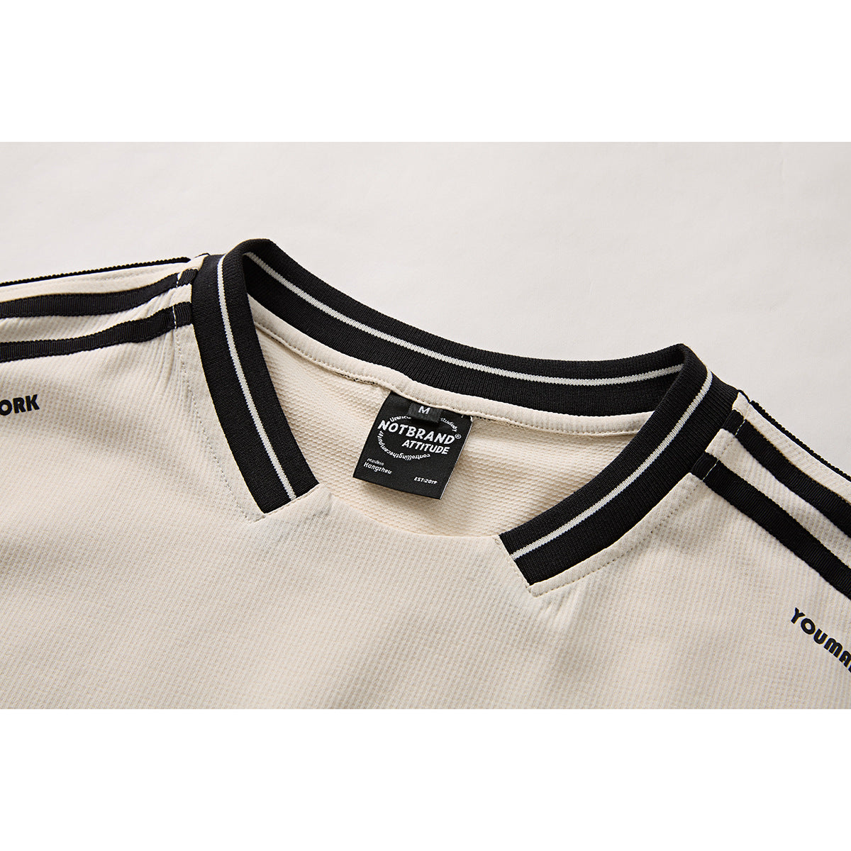 Close-up of an ivory shirt’s black-and-white striped V-neck ribbing, shoulder stripes, and inside neck label.