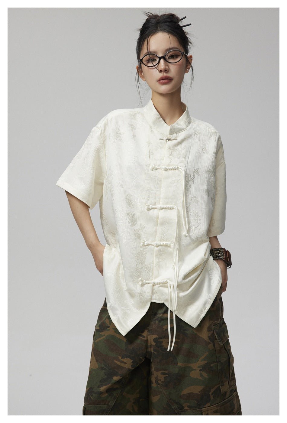 Model wearing an ivory short-sleeve floral jacquard shirt with a stand collar and frog closures.