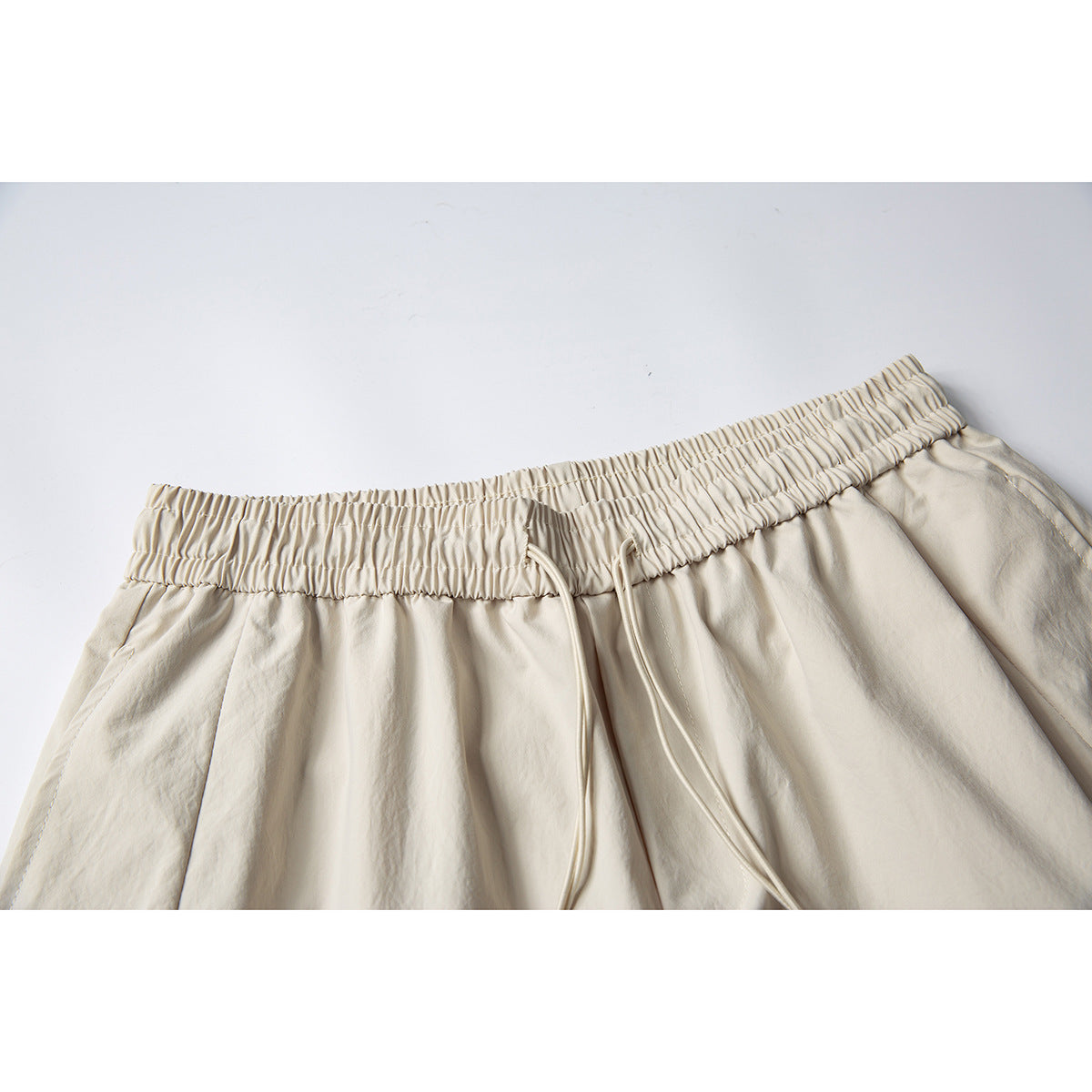 Close-up of cream shorts showing the gathered elastic waistband, drawstring, and upper seams.