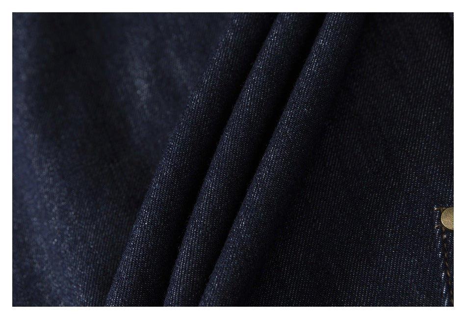 Close-up of dark indigo denim folds with a partial brass-colored button at the edge.