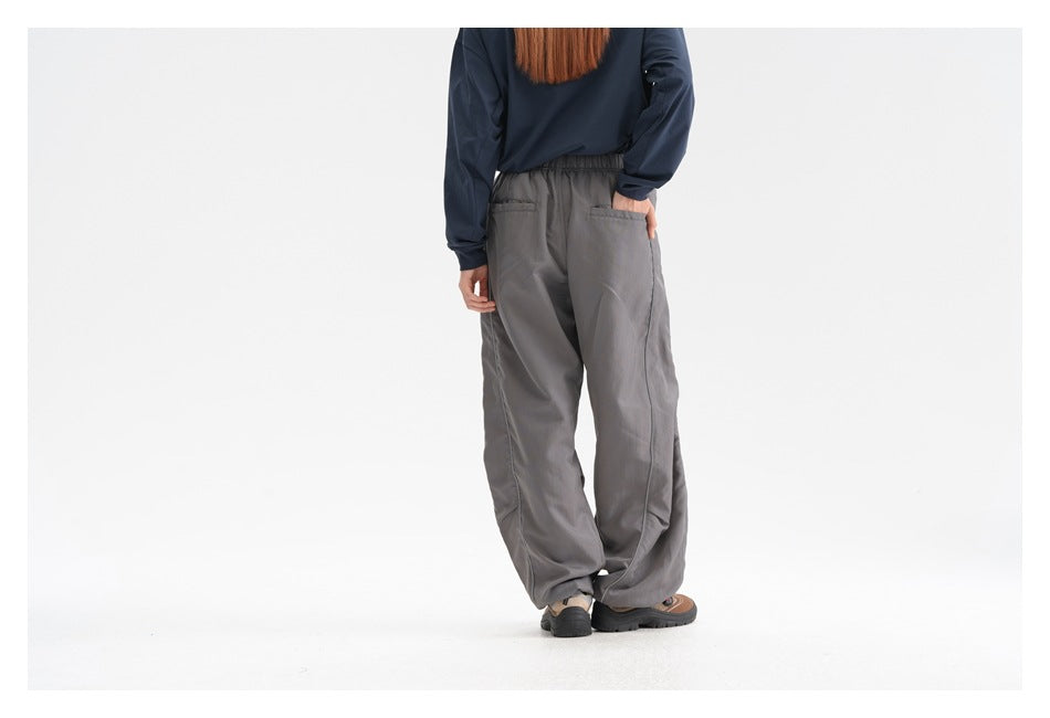 Rear view of a model wearing loose gray pants with an elastic waist and two back pockets.