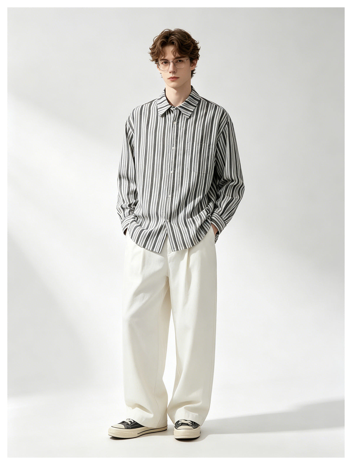 A man wears a white button-up shirt with black vertical stripes and loose white trousers.