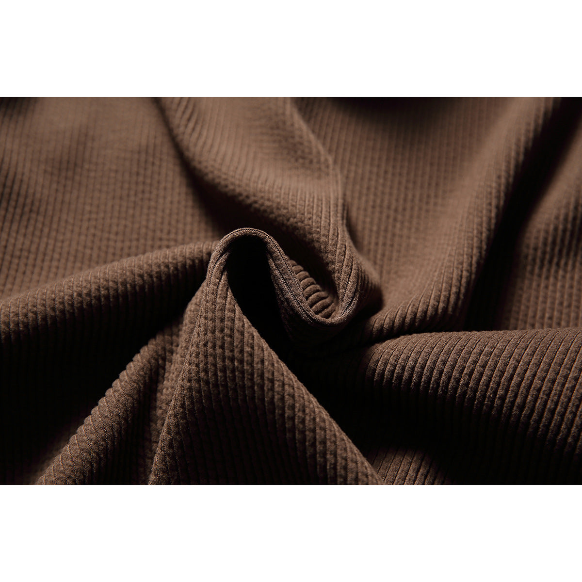 Close-up of brown textured hoodie fabric arranged in folds, showing its raised ribbed surface.