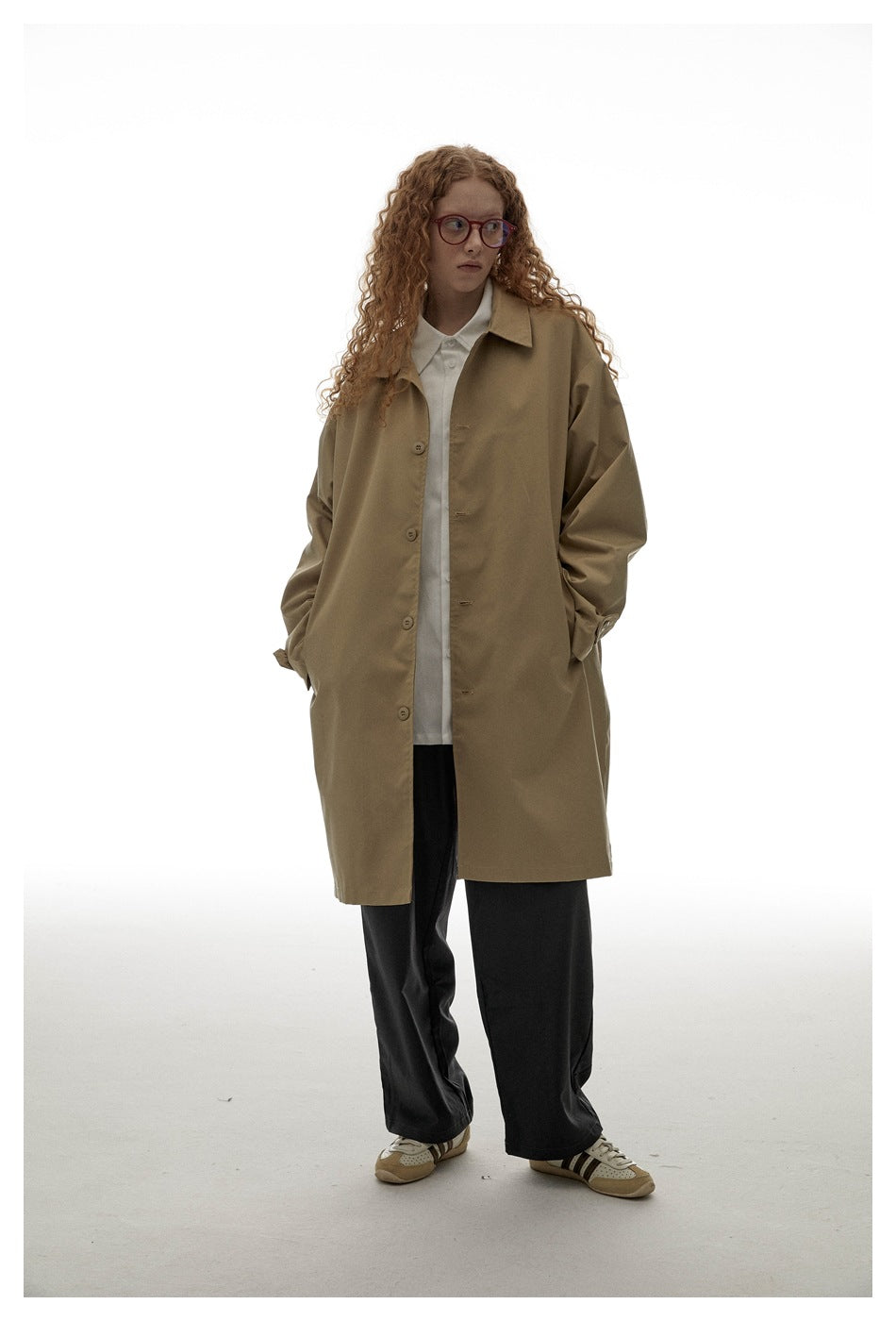 Model wearing a loose tan button-front coat over a white shirt and black wide-leg trousers.