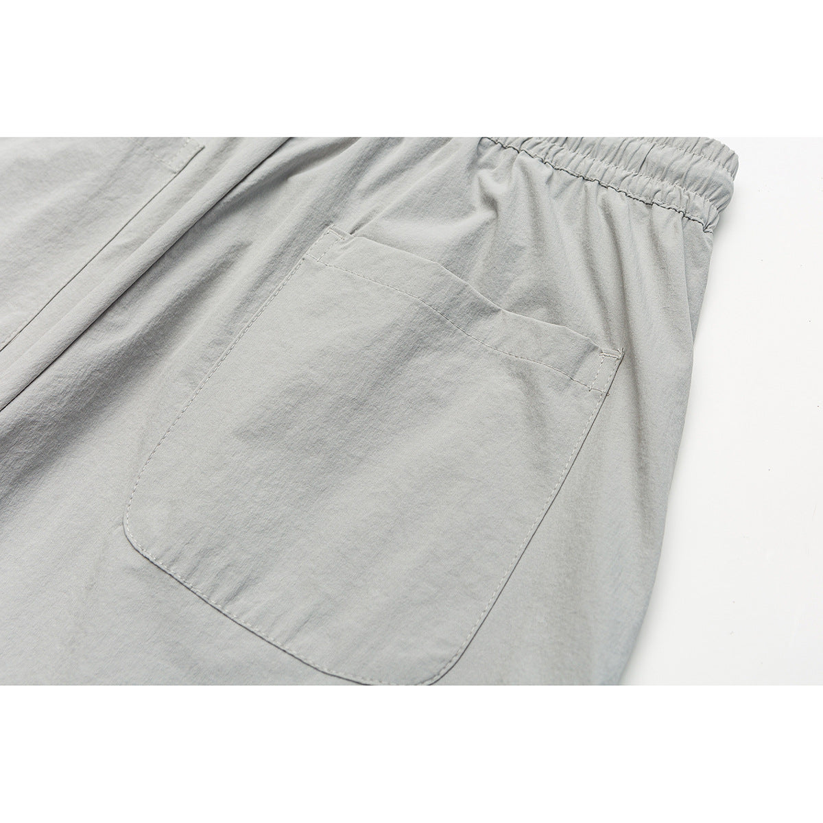 Close-up of a large patch pocket and elastic waistband on light gray trousers.