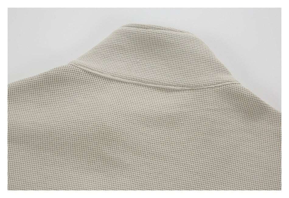 Close-up of the collar and upper back of a light beige-gray garment with a textured knit pattern.
