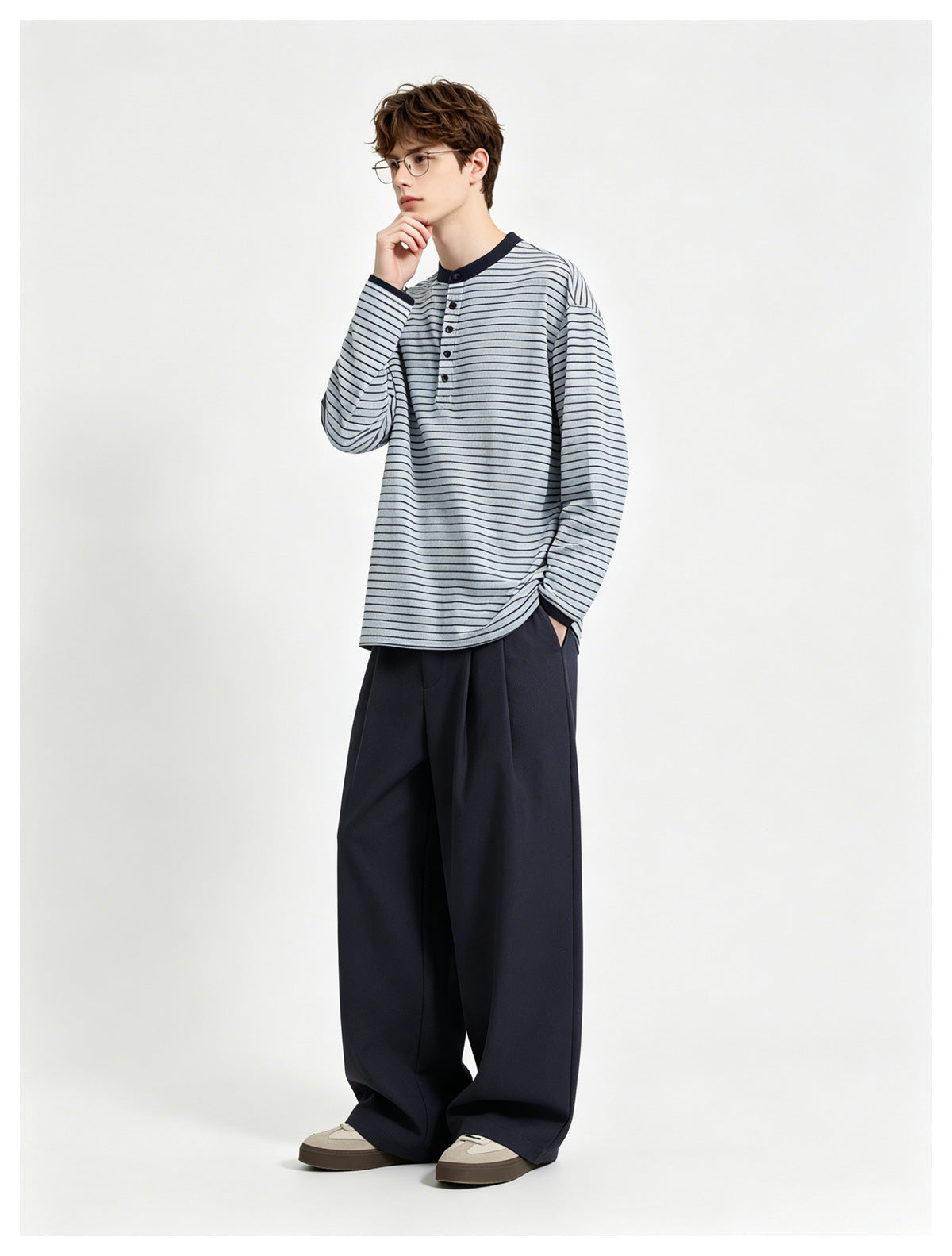Model in a blue striped Henley top with navy collar and cuffs, wide navy trousers and sneakers, standing in a pose
